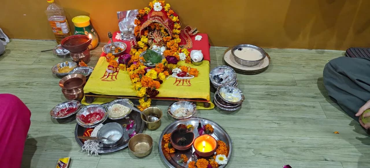 A puja set out on the floor: a marigold-covered altar, a lit oil lamp and bowls of offerings