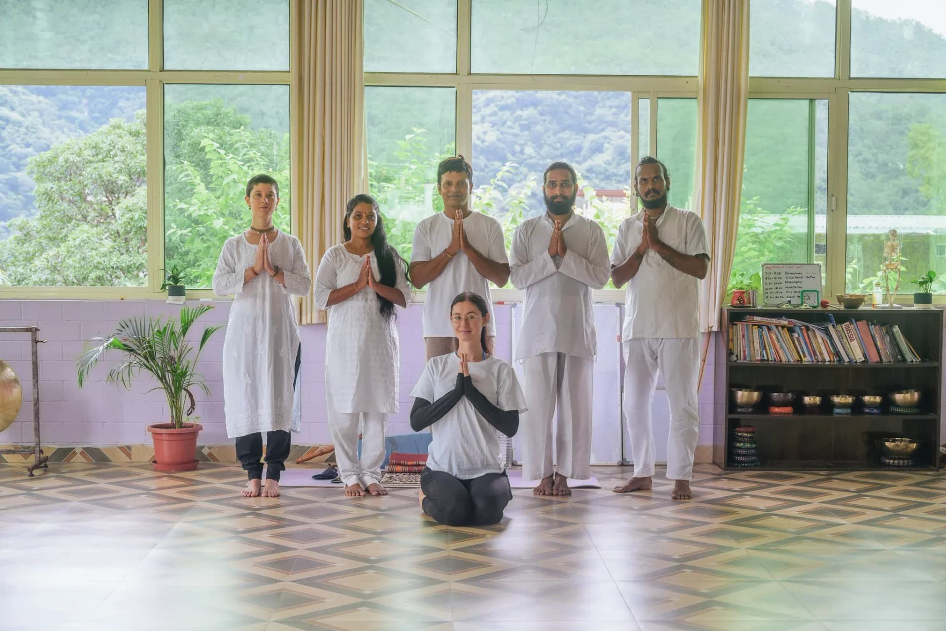 Students and teacher in white greet with namaste hands in the Anantadrishti Yoga shala in Rishikesh