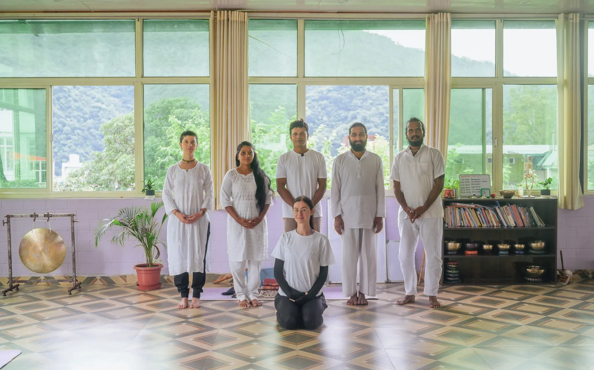 Students and teacher in white pose together in the Anantadrishti Yoga shala in Rishikesh