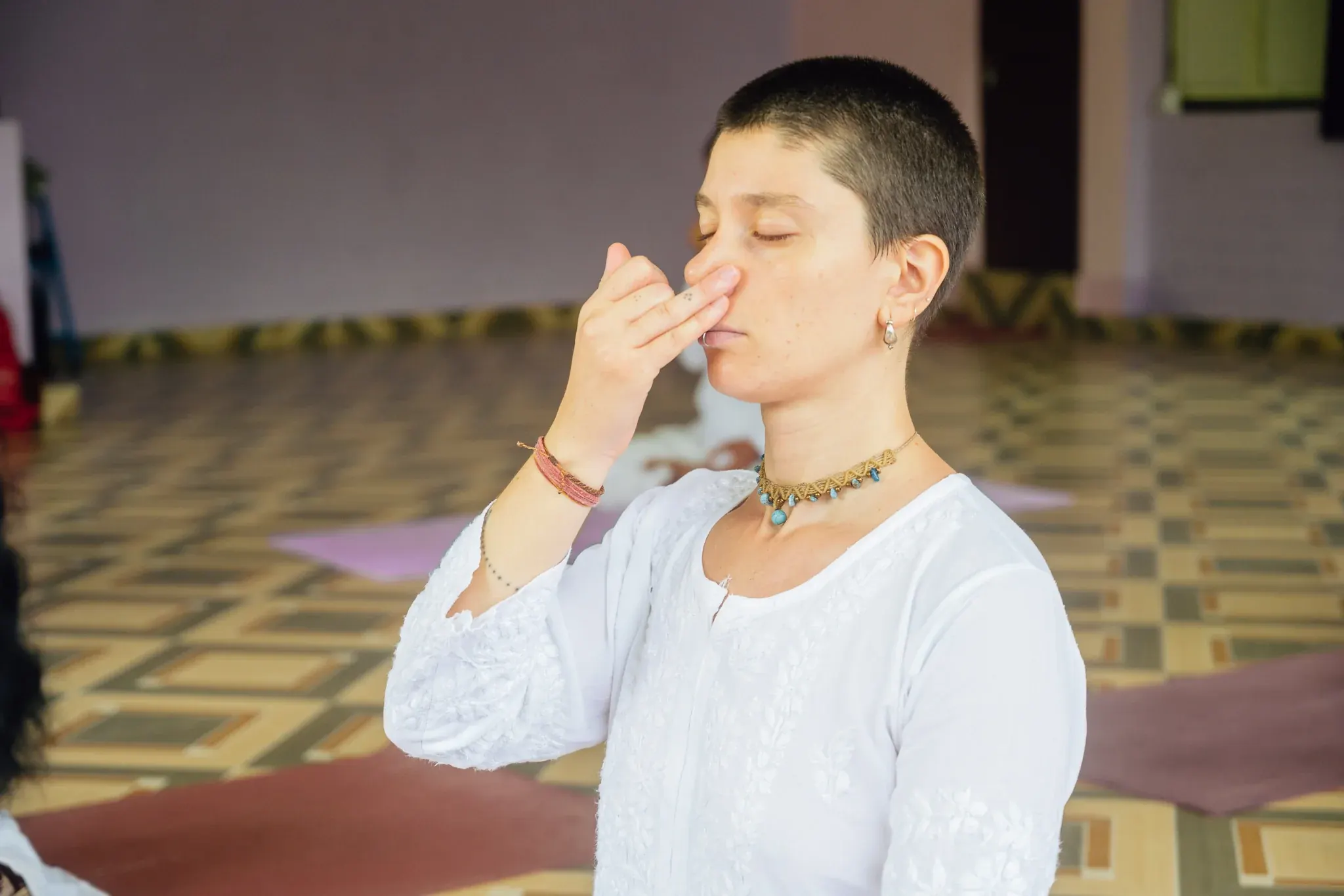 Close-up of a student practicing Nadi Shodhana with the right hand at the nose, eyes closed, in Rishikesh