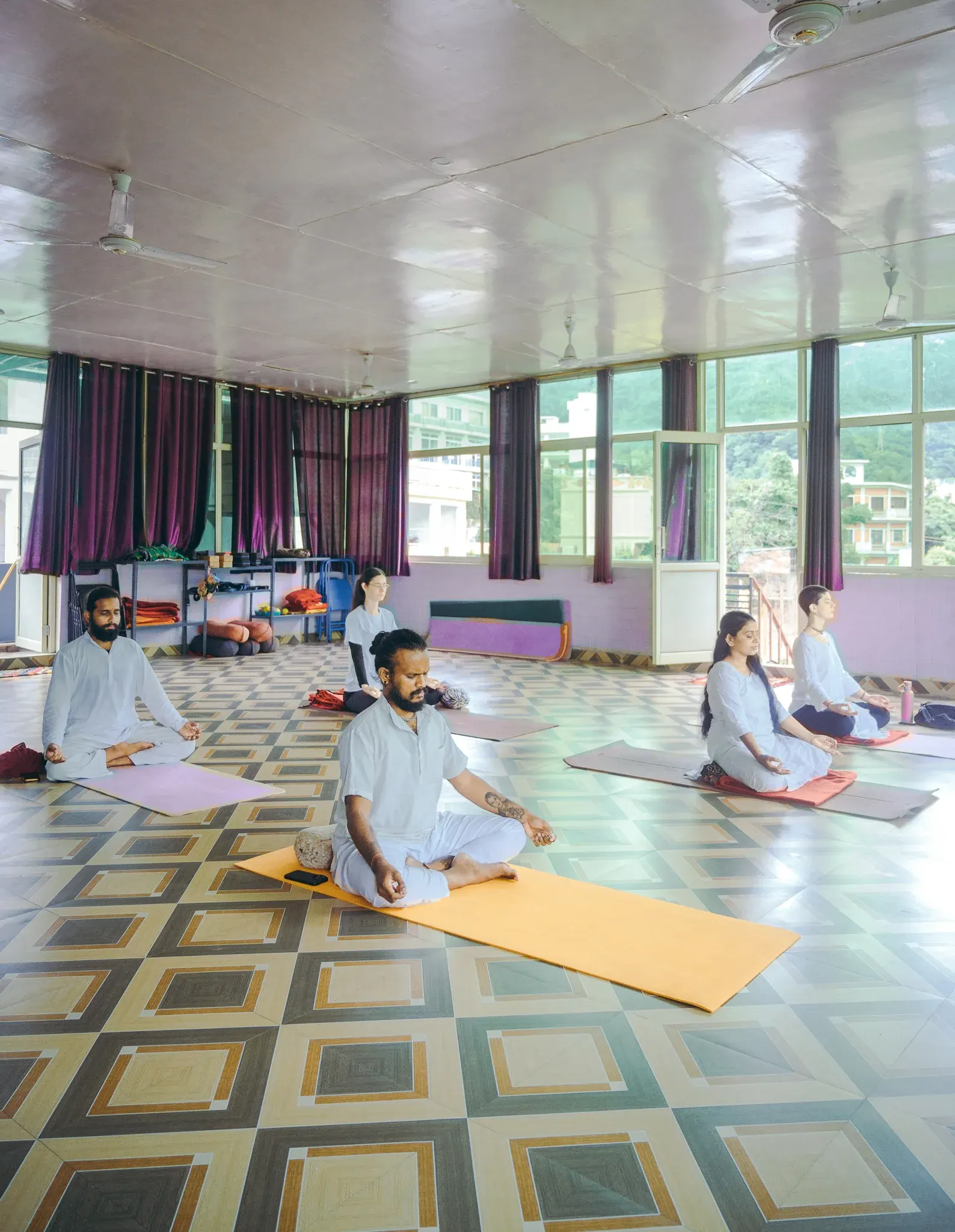 Pranayama students in white sit in meditation with chin mudra in a bright yoga hall in Rishikesh