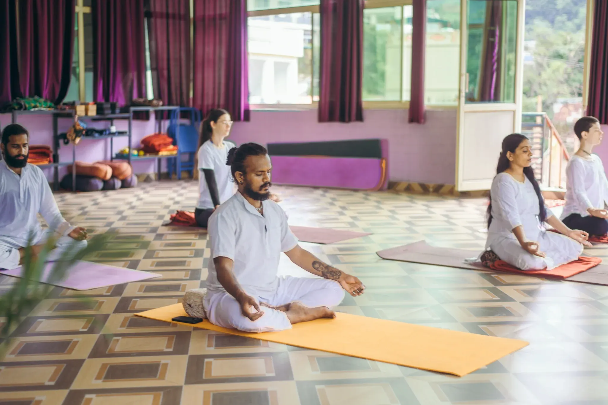 Students in white meditating cross-legged in chin mudra in a yoga shala in Rishikesh