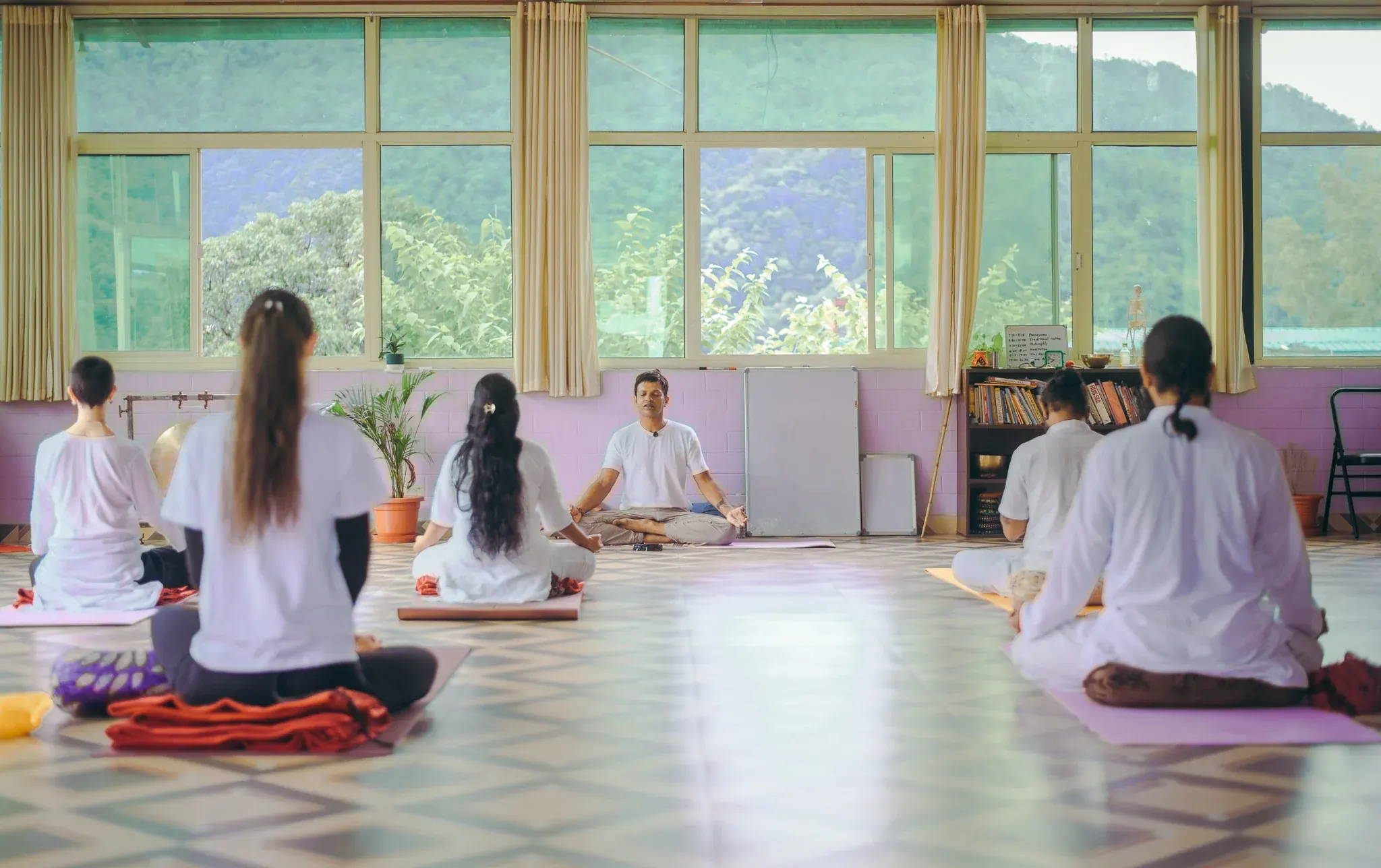 숲이 우거진 초록 언덕을 마주한 리시케시 요가 샬라에서 앉아 있는 학생 다섯 명을 이끄는 교사