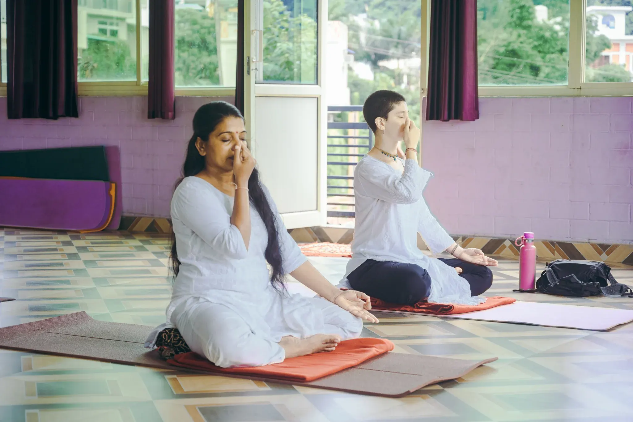 Two women practice Nadi Shodhana with the right hand at the nose and chin mudra in a Rishikesh yoga shala